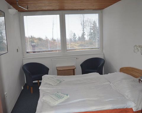 Dvojlôžková izba, pod oknom dve kreslá a stolík.